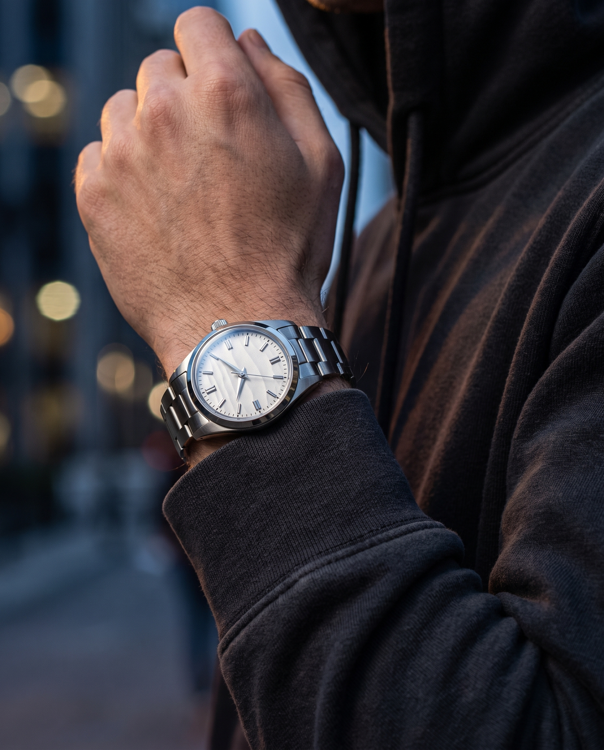 The Meridian Watch worn on wrist, dark hoodie, night city bokeh